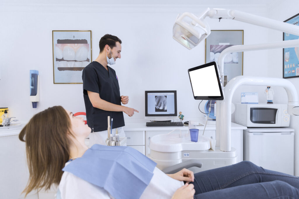 male dentist explaining teeth x ray screen female patient lying dentist chair